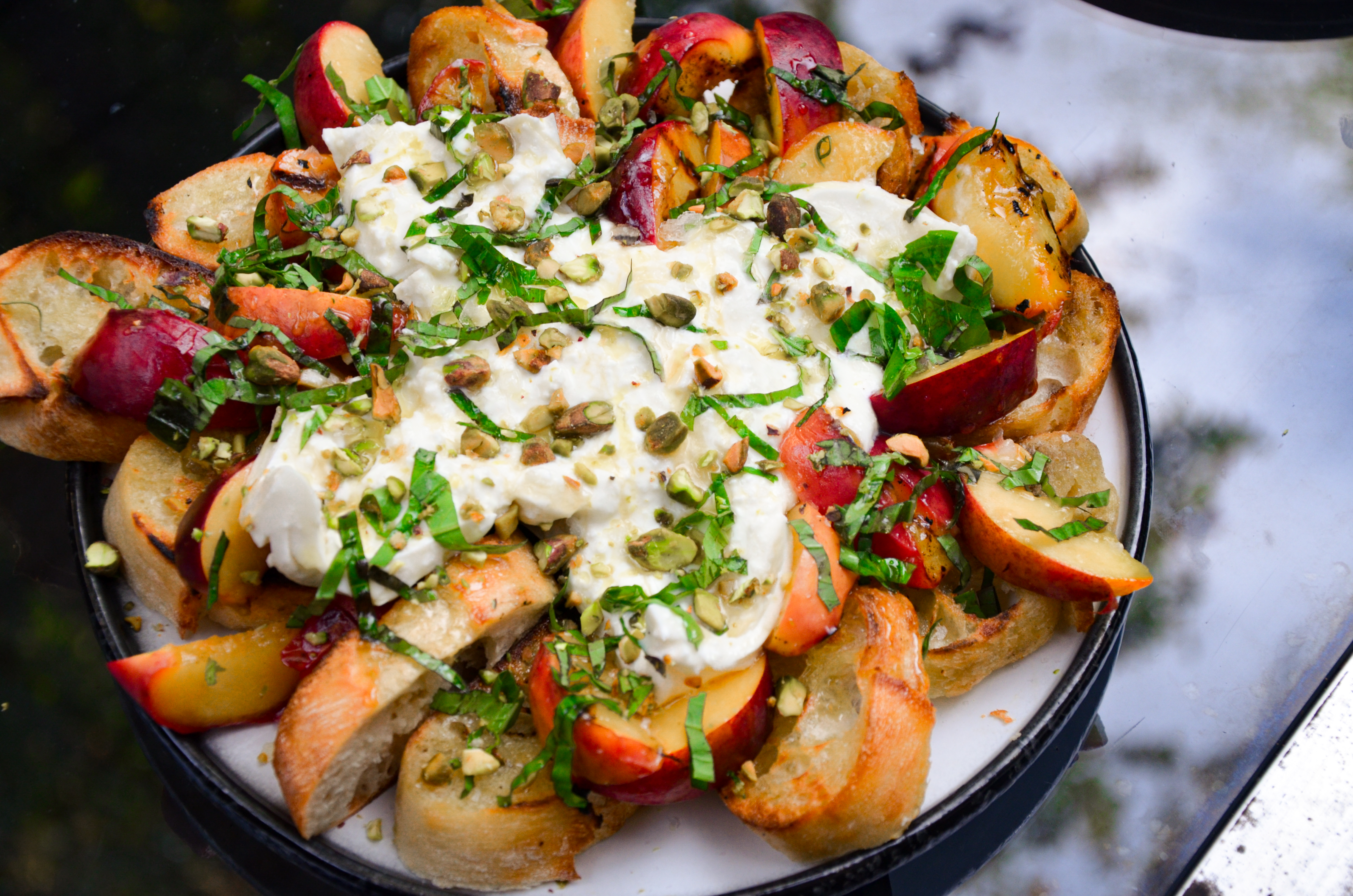 peaches, crostini and burrata arranged on a plate with basil and pistachios sprinkled