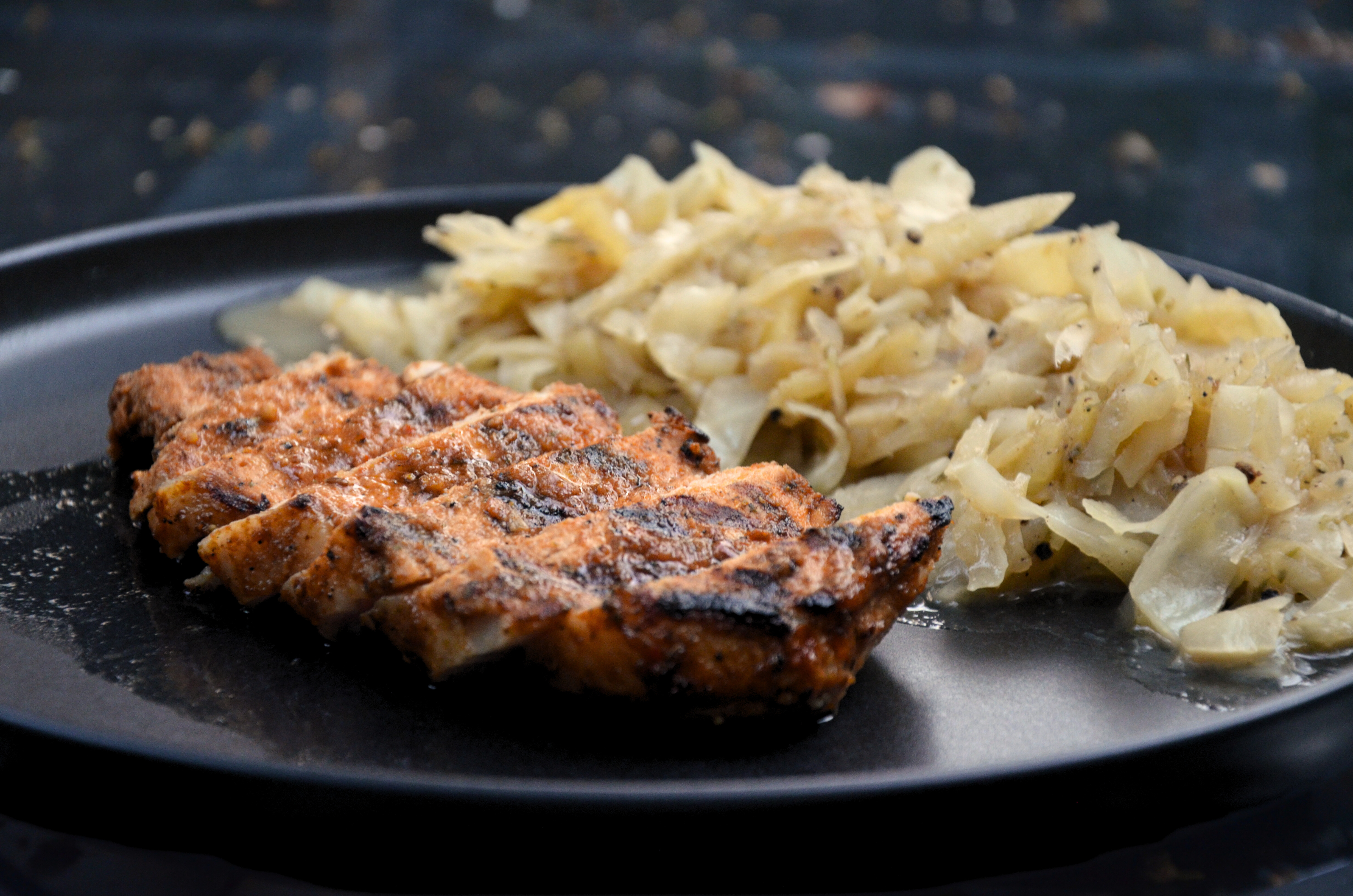 Grilled porkchop on a black plate with braised cabbage and apples