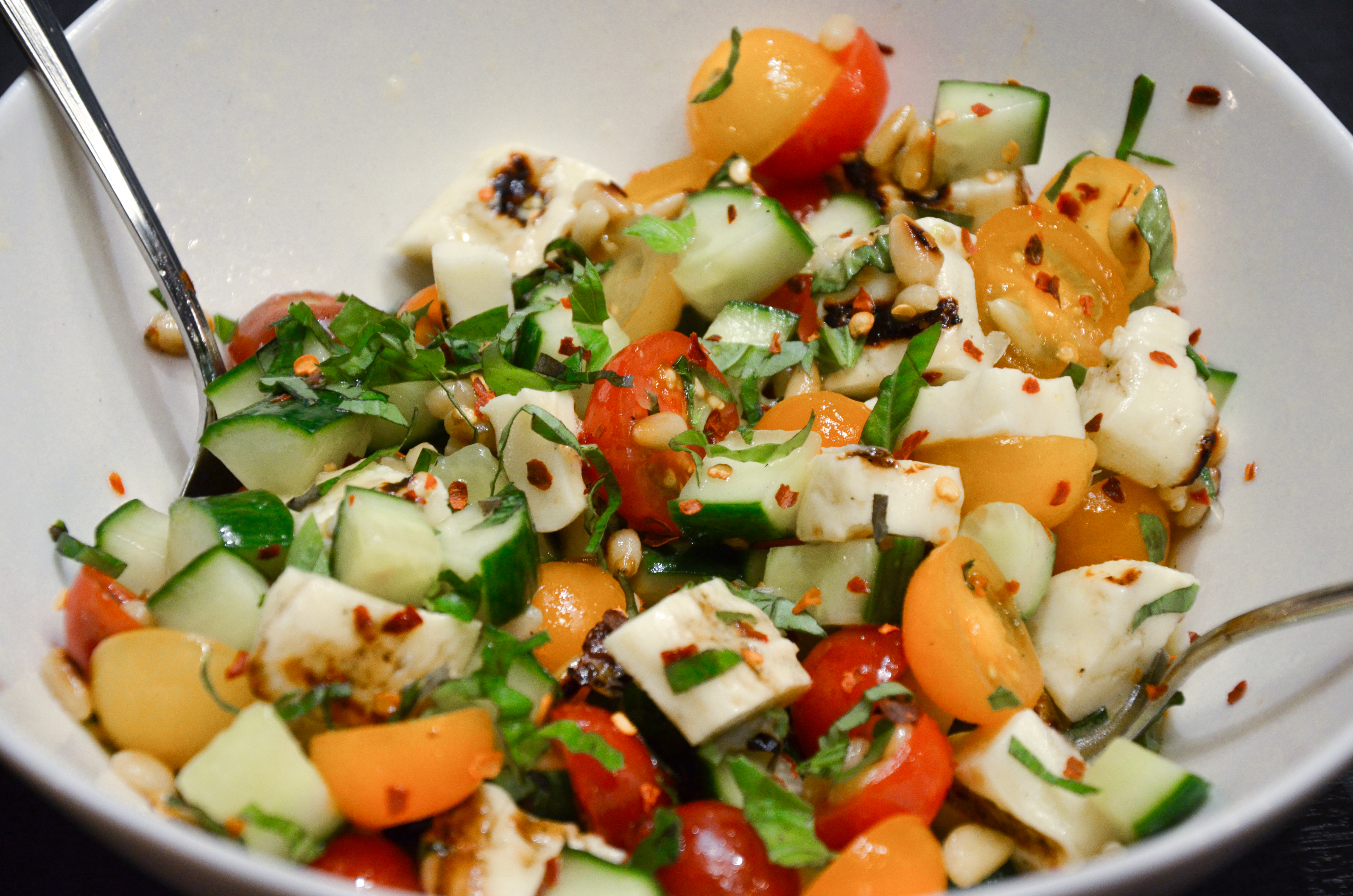 A salad with grilled halloumi, pine nuts, tomatoes, cucumbers, red pepper flakes and strips of basil.